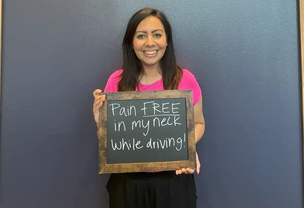 Limitless Chiropractic female patient smiling while holding a sign that says “After 2 weeks I can function better at work & at the gym!” — showing improved mobility and performance through chiropractic care in Alliance, Fort Worth.